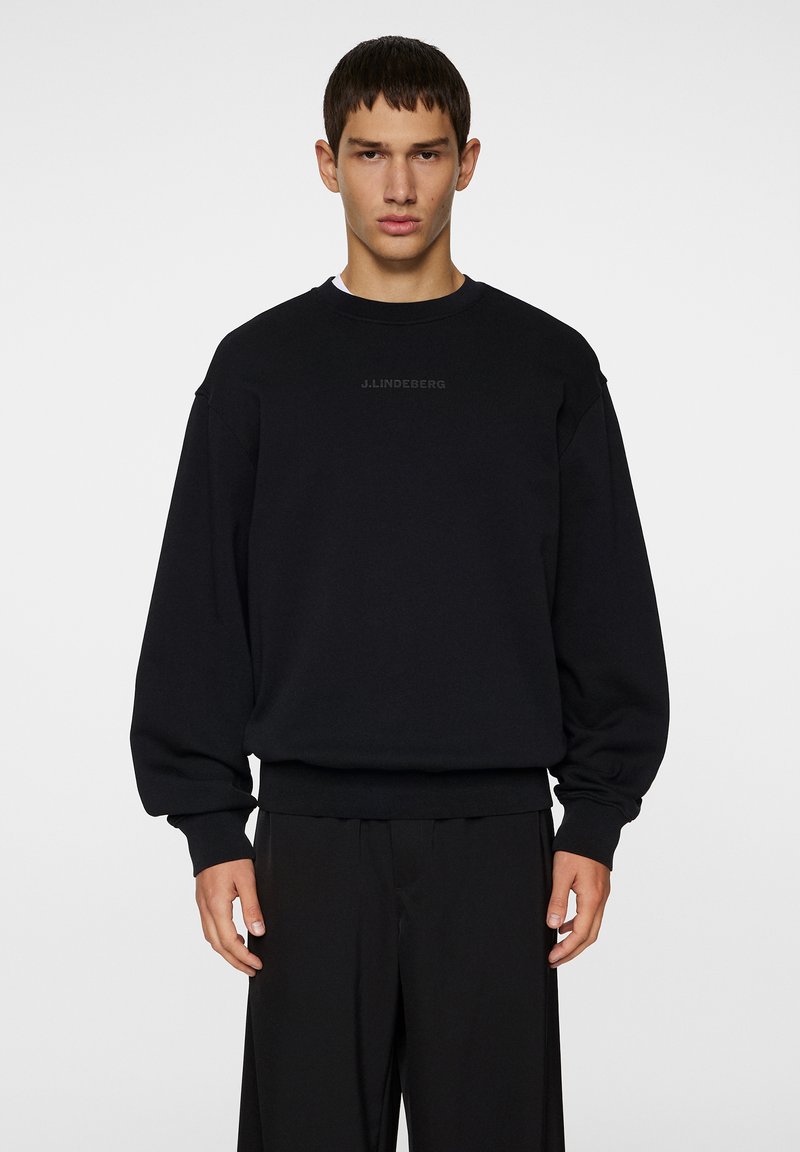 Sort sweatshirt med rund hals, lange ærmer og afslappet pasform. Har diskret logo tekst på brystet samt ribbede kanter og ærmer.