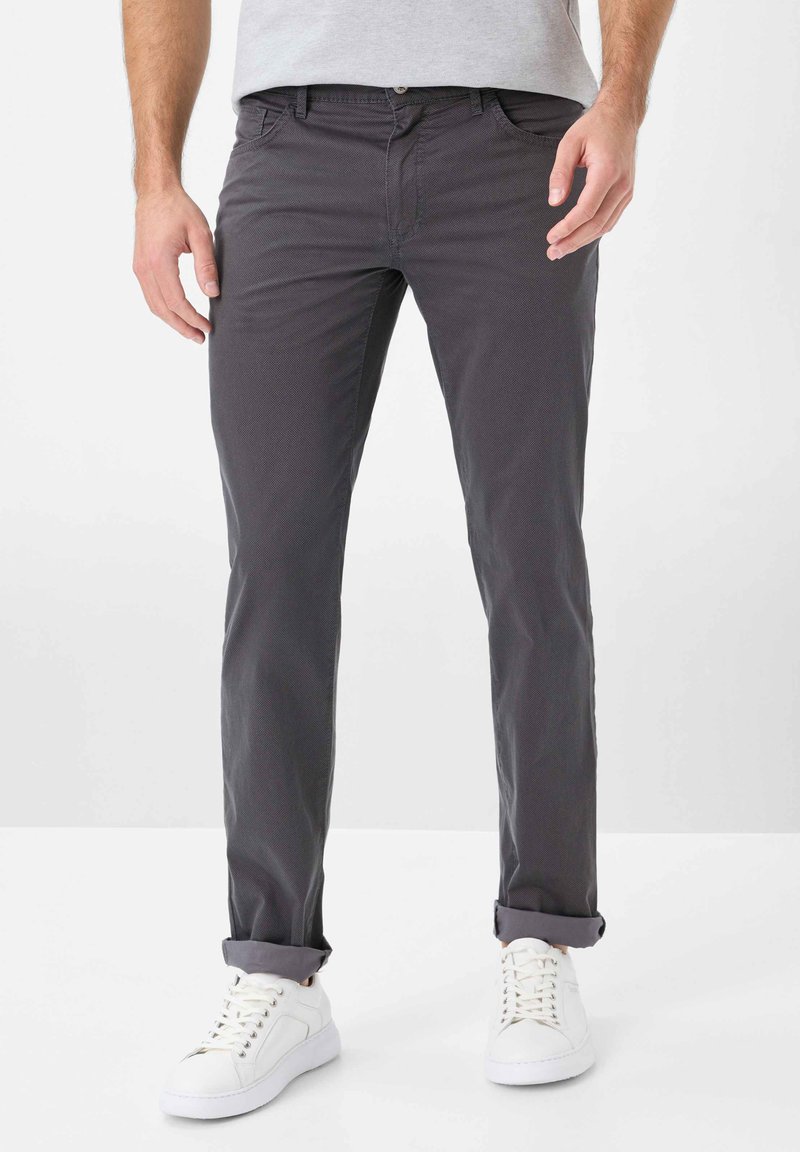 Graue Baumwollhose mit slim fit, aufgerolltem Saum und Fronttaschen. Kombiniert mit weißen Sneakern und einem grauen T-Shirt.