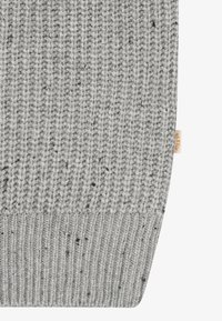 Šedá pletená tkanina s texturovaným žebrovým vzorem, s černými tečkami a malou nášivkou na okraji. Měkký, teplý vzhled.