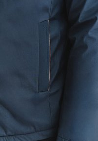 Navy blue jacket z detalem strukturalnej kieszeni z przeszytymi brzegami i kontrastującym akcentem miedzianym. Gładka faktura, lekkim materiał.