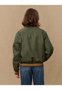 Grüne Bomberjacke mit vertikalen orangenen Streifen, elastischem Bund und Bündchen. Entworfen mit einer glatten, glänzenden Textur.