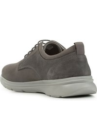 Chaussure en suède gris avec une silhouette basse, un bout rond et un design à lacets. Présente une tige texturée et une semelle contrastante gris clair.