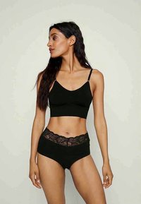 Črn bralet z tankimi naramnicami, v kombinaciji z visokimi črnimi hlačkami, ki imajo čipkast pas. Gladka tekstura tkanine.