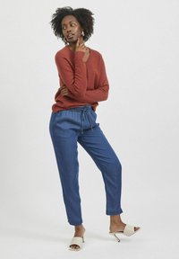 Pull en maille couleur rouille avec un col en V, associé à un pantalon bleu clair ample doté d'une taille élastique et d'un cordon de serrage. Sandales à talons beiges.