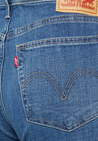 Dark blue denim jeans featuring a signature Levi's red tab, gold stitching, and distinctive curved pocket design on the back.