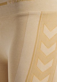 Beige Leggings mit gerippter Textur und einem gemusterten Design mit Zickzackmotiven. Der Stoff hat eine weiche Oberfläche und eine enganliegende Passform.