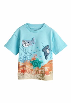 Világoskék rövid ujjú póló vízi állat applikációkkal: bálna, teknős, hal és rák, homokos óceánfenék háttérrel.