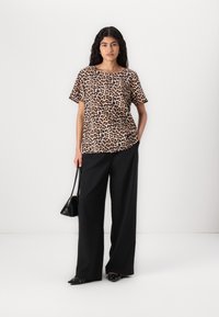 Kortermet topp med leopardmønster laget av lett stoff, kombinert med brede svarte bukser og en liten svart håndveske.