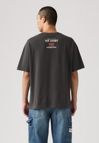 Camiseta de corte oversize en gris oscuro, hecha de algodón, con un diseño de Toy Story impreso en blanco y rojo en la parte trasera, con mangas cortas y cuello redondo.
