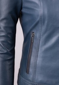 Blue leather jacket with a fitted design, featuring a zippered pocket and woven textured hem. Smooth texture and sleek silhouette.