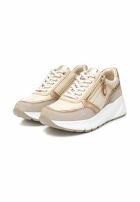 Zapatillas beige y doradas con un acabado texturizado, que cuentan con un detalle de cremallera, cordones blancos y una suela blanca gruesa y elevada.