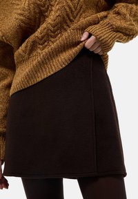 Jupe en polaire marron à coupe droite et détail de couture sur le côté, associée à un pull texturé moutarde avec un motif en torsades.