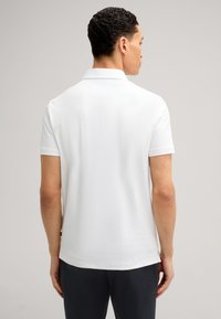 Witte polo met korte mouwen, van een zachte stof, met een klassieke kraag en zijsplitten. De stof lijkt lichtgewicht en ademend te zijn.