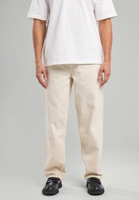 Beige cotton pants with a straight cut, lightweight fabric, and a smooth texture, paired with black shoes and a plain white T-shirt.