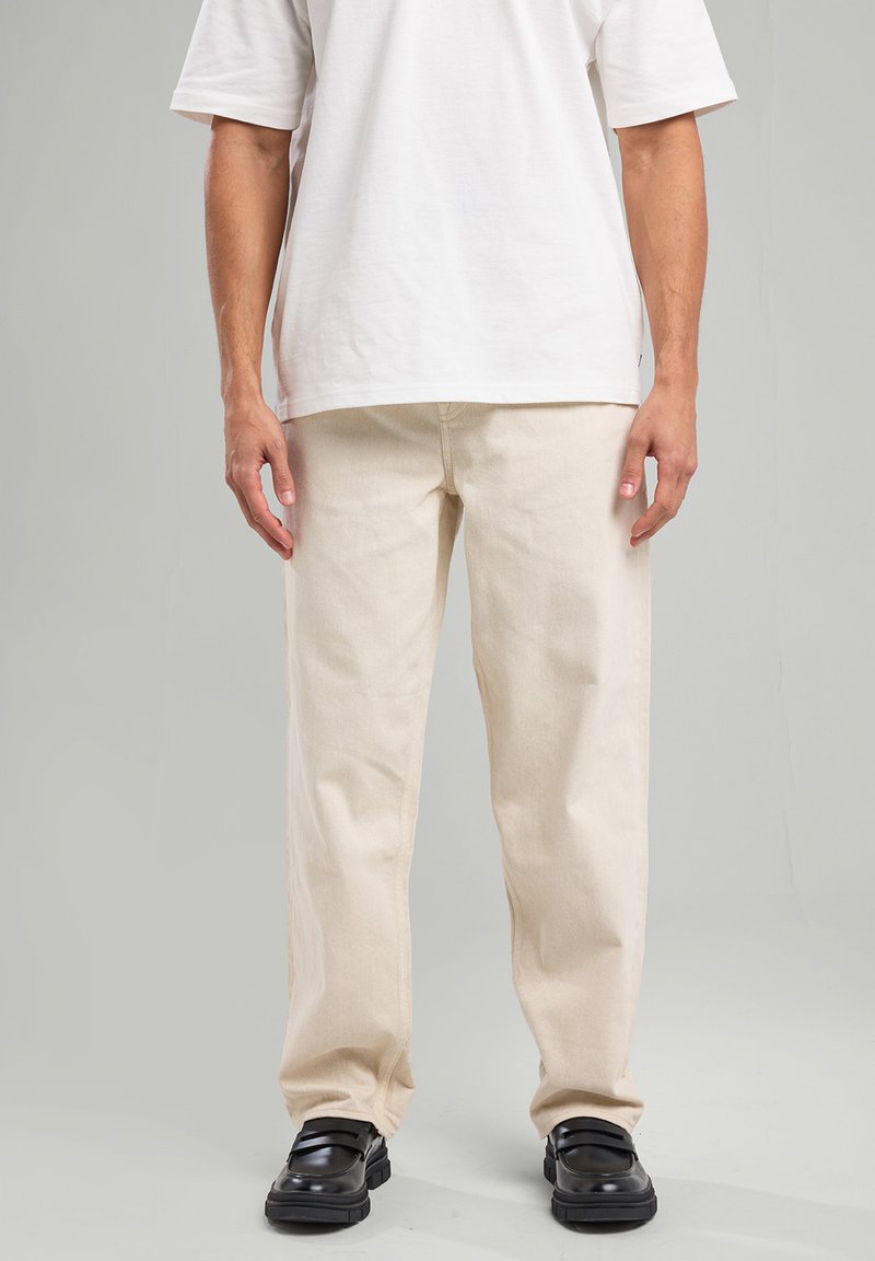 Beige cotton pants with a straight cut, lightweight fabric, and a smooth texture, paired with black shoes and a plain white T-shirt.