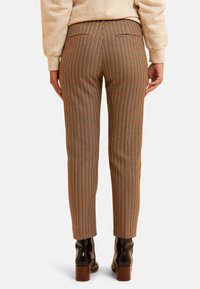 Los pantalones marrones a cuadros tienen un corte ajustado, dos bolsillos traseros y se combinan con botines negros brillantes y un suéter ligero.
