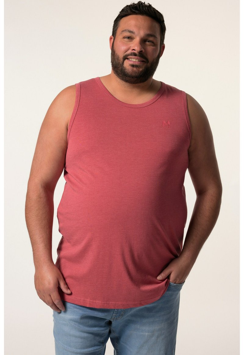 Rotes Trägershirt aus Baumwollmischung mit Rundhalsausschnitt und subtiler Logo-Platzierung auf der linken Brust. Kombiniert mit hellblauen Jeans.