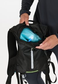 Black hydration backpack with mesh back, zipper closure, and bright green accents. Contains a blue hydration reservoir with a tube visible.
