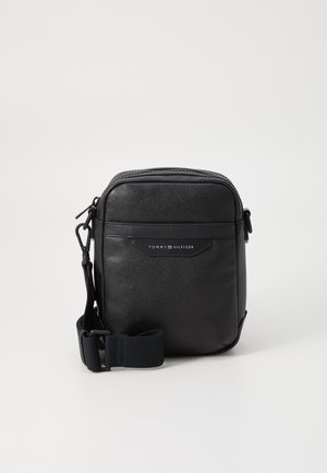 Black leather crossbody bag with textured finish, zip closure, adjustable strap, and embossed logo detail on front. Compact rectangular shape.