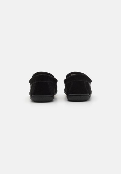 Must võipli sees olevad mustad nubukist kingad ümarate seljaga, pehme tekstuur ja paindlikud kummitald. Minimalistlik disain, ilma nähtava riistvarata.