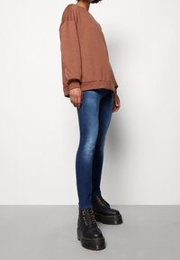 Brun oversized sweatshirt, blå skinny jeans och svarta kraftiga snörboots med guldhårdvara. Enkelt, avslappnat outfit med en ledig passform.