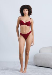 Το σετ εσώρουχων σε μπορντό περιλαμβάνει ένα padded σουτιέν με λεπτές τιράντες και αντίστοιχες ψηλόμεσες βερμούδες. Μαλακή υφή με ελάχιστα σχεδιαστικά στοιχεία.