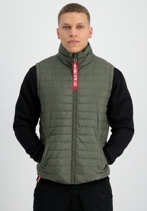 Grøn quilted vest med høj krave, to sidelommer, lynlåslukning og rød mærke detalje, båret over en sort langærmet skjorte.