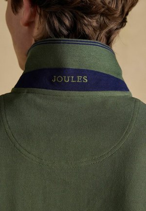 Henkilö, joka pukeutunut vihreään poolopaitaan, jossa on tummansininen kauluksen reunus, ja kauluksen takana lukee kirjailtuna "JOULES".