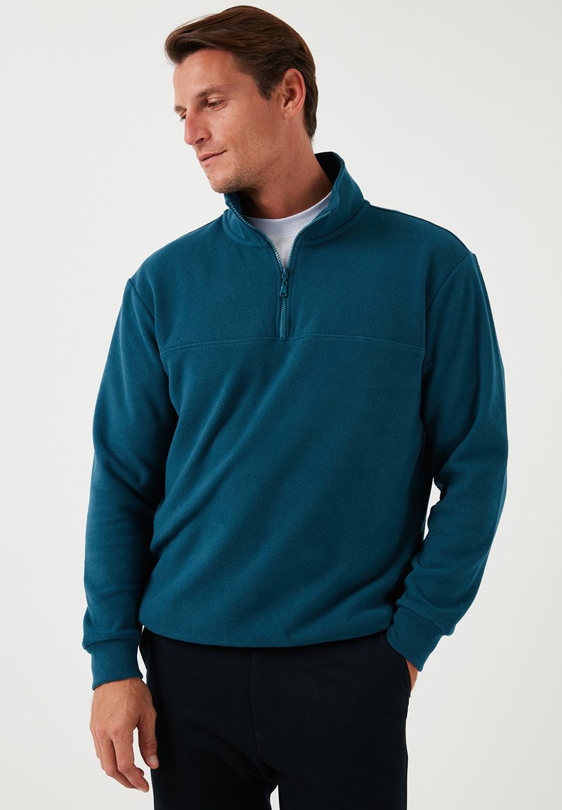 Türkiser Fleece-Pullover mit Reißverschlusskragen, langen Ärmeln und glatter Textur. Verfügt über eine horizontale Nahtdetails auf der Brust.