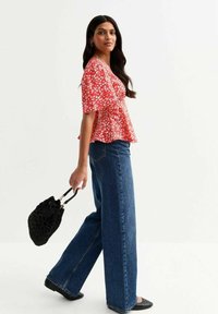 Red floral blouse with short sleeves, peplum design; paired with wide-leg blue jeans and a black woven handbag. Smooth texture, casual fit.