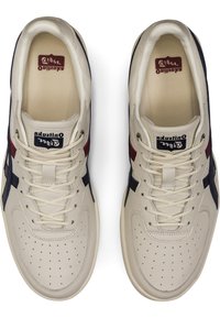 Beżowe skórzane sneakersy z granatowymi i czerwonymi akcentami, na sznurowanie, z perforowanym noskiem oraz logo marki na języku i wkładce. Gładka tekstura.