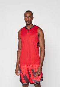Top deportivo rojo sin mangas con un escote negro, combinado con pantalones cortos rojos que presentan un atrevido patrón de relámpago negro y detalles en blanco.