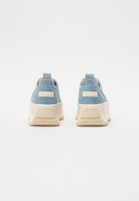 Sneakers in denim blu con suola beige spessa, dotati di un pratico passante posteriore e di una patch con logo sul tallone. Design minimalista, texture liscia.