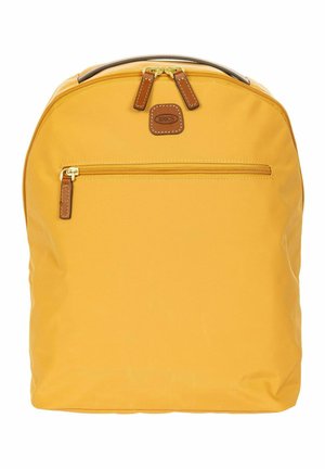 Sac à dos jaune avec poche avant zippée, tirettes de fermeture éclair en cuir marron et poignée supérieure, marqué d'un petit patch en cuir.