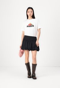 T-shirt blanc avec le texte "PARIS" et un graphisme floral, jupe noire à volants, pochette rose et bottes marron jusqu'aux genoux avec boucles.