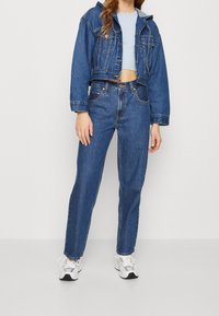 Džínsová bunda ve středně modré barvě s krátkým střihem, doplněná o džíny s vysokým pasem. Bílé tenisky s detaily. Hladká džínová textura.