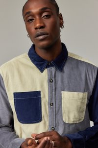 Cordfløyelskjorte i grått, marineblått og lys beige; har en knapp-front, kontrastfarget lommer og en strukturert krage.