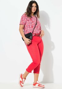 Röd mönstrad t-shirt, röda slim-fit byxor och röd-och-vit sneakers. Tillbehören inkluderar en liten svart axelväska och ett rött bälte.