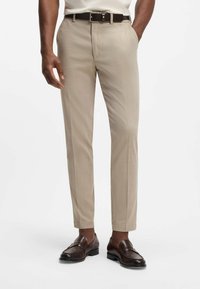 Beige op maat gemaakte broek van gladde stof, met een platte voorkant, zijzakken en een slanke pasvorm, gecombineerd met bruine lederen loafers.