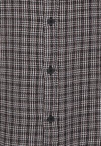 Strukturiertes schwarz-weißes Hemd mit Knöpfen und kariertem Muster, mit einem auffälligen schwarzen Knopf vorne.