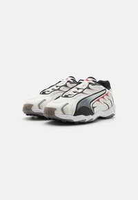Witte en zwarte sportieve schoenen met een bovenwerk van mesh, dynamische textuur, reflecterende accenten en een rubberen zool. De veters hebben een dunne zwarte streep.