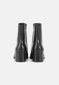 Mustad nahast pahkluu saapad, sileda viimistluse, ümarate varvaste ja külgmise lukuga, pakse plokksangana stabiilsuse tagamiseks.