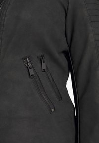 Giacca nera con una trama liscia, dotata di due tasche con zip e accenti a coste verticali sulle spalle.