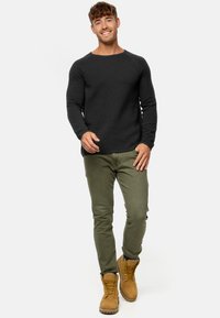 Mørkegrå, ribbet langærmet skjorte; olivengrønne slim-fit bukser; lysebrune snørebåndsstøvler; afslappet stilling på en hvid baggrund.