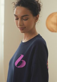 Navy blue sweatshirt with a large pink embroidered "6" on the chest, featuring a classic crew neckline and soft fabric texture.