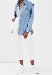 Chemise en denim bleu clair au design surdimensionné, avec une poche avant et un texte brodé. Associée à un pantalon blanc retroussé et des bottes blanches à lacets.