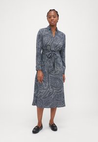 Abito lungo a maniche con motivo paisley, scollo con colletto, vita con fascia avvolgente e gonna svasata. Mocassini neri completano l'outfit.