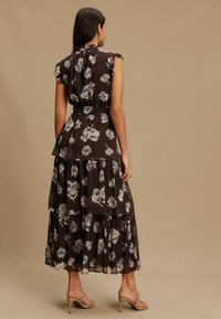 Virágos maxi ruha áttetsző anyagból, fodros ujjakkal, rétegzett szoknyarésszel és elasztikus derékrésszel. Sötétbarna alapon világos virágmintával.
