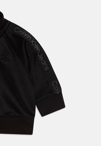 Felpa nera con colletto alto, dotata di logo ricamato e testo "Calvin Klein Jeans" lungo la manica in grigio. Tessuto dalla texture morbida.