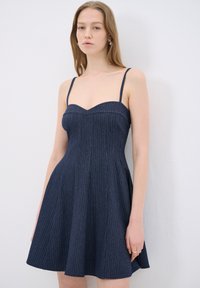 Laivonsininen farkkumekko ohuilla olkaimilla, sydänpääntie ja pystysuorat raidat. Laajakärki ulottuu vyötärön alapuolelle.